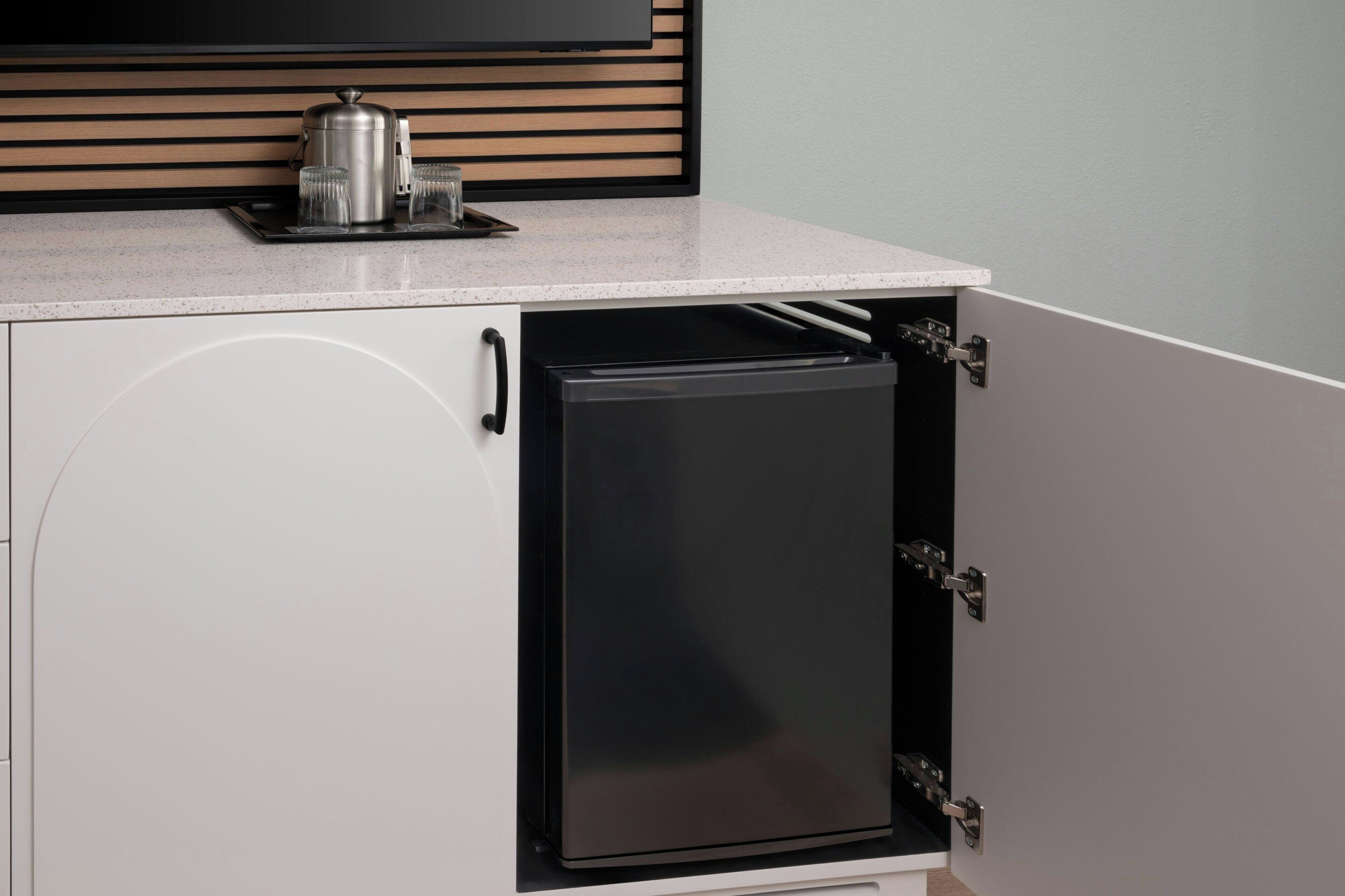 A compact kitchen with a built-in refrigerator, a coffee maker, and a microwave on the countertop.