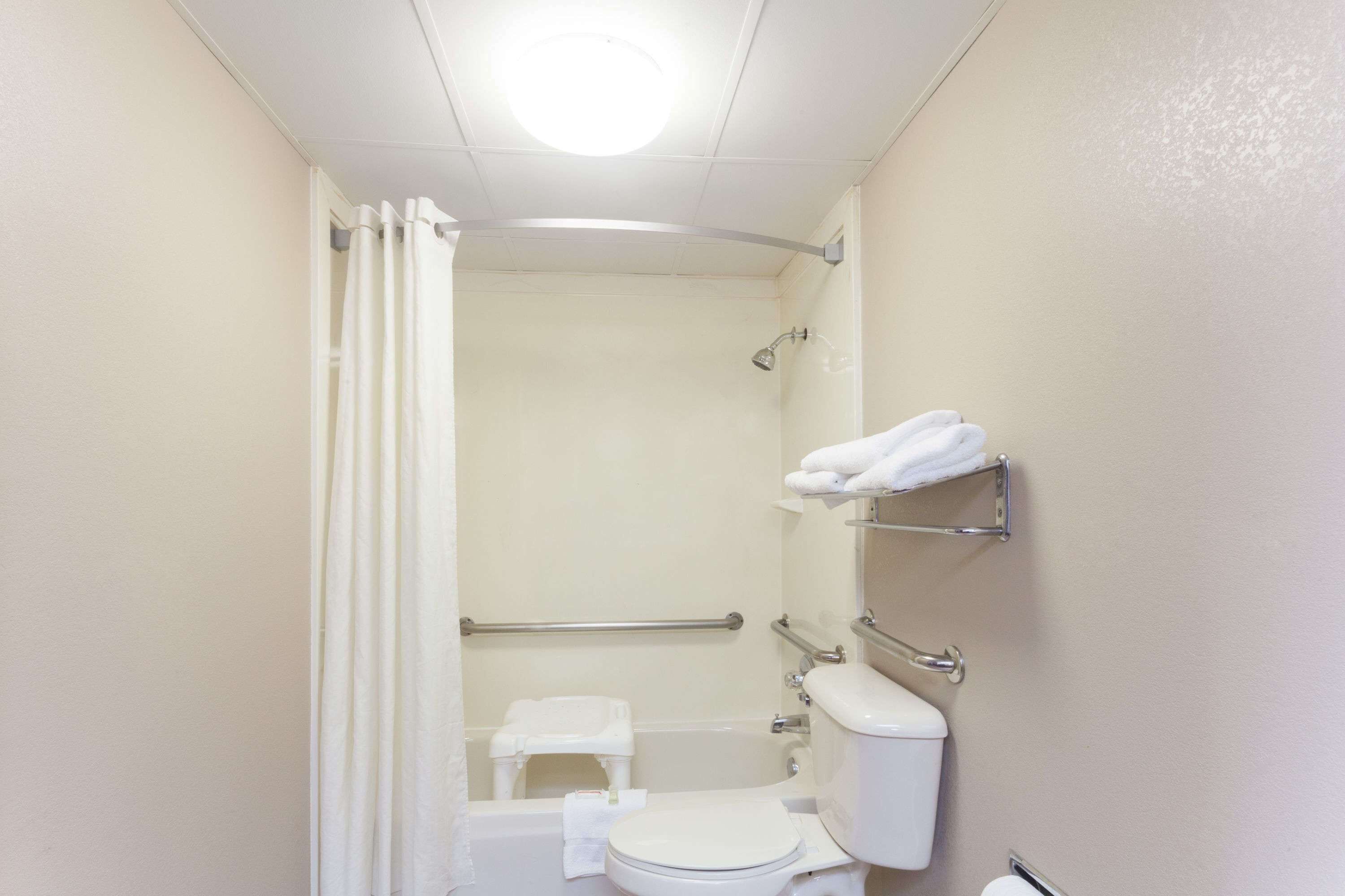 A small, white bathroom with a shower, toilet, and a shelf with towels.