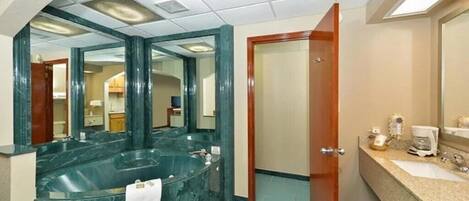 Un baño con una amplia bañera de mármol, una zona de lavamanos separada y un espejo.