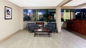 A spacious lobby with a reception desk, two armchairs, a coffee table, and a large window offering a view of the cityscape.