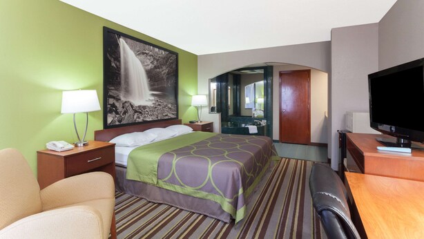 A hotel room with a bed, a desk, a TV, a mirror, and a bathroom visible through an archway.