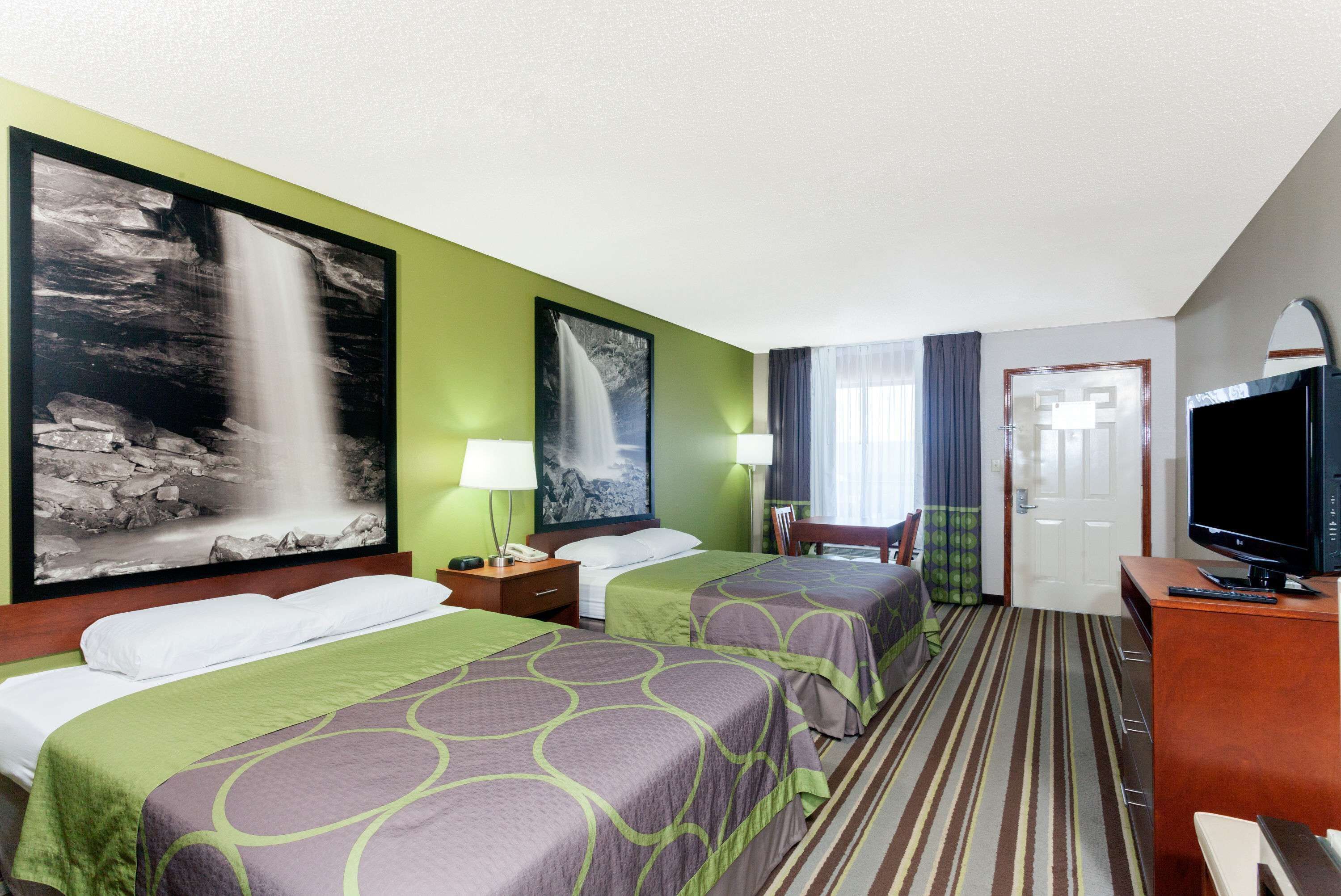 Habitación de hotel con dos camas, televisor, escritorio y puerta al baño.