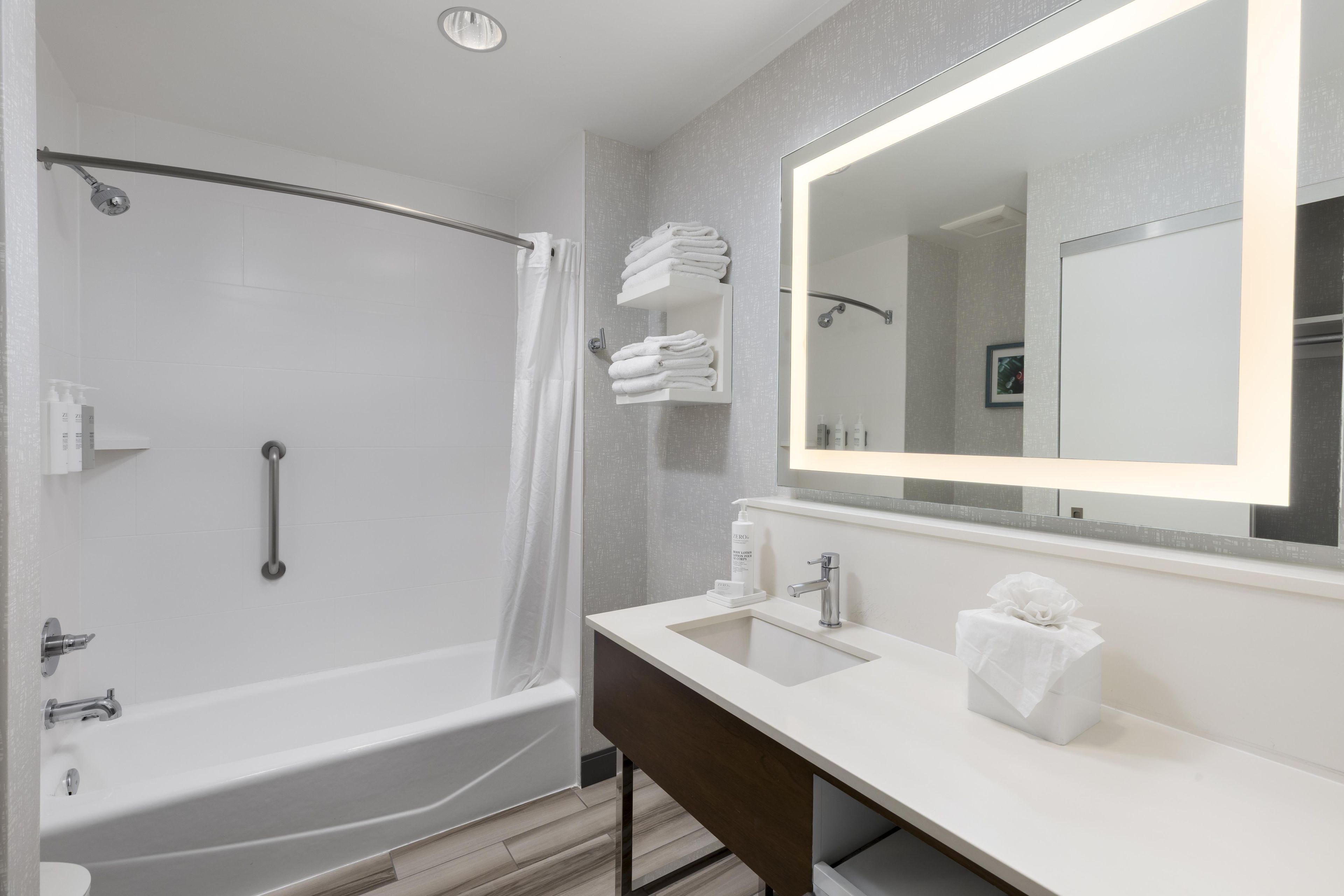 Un baño moderno con ducha a nivel, tocador con espejo y un perchero para toallas.