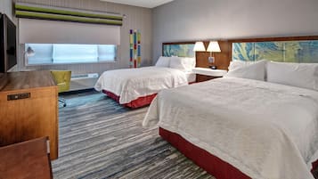 A hotel room with two beds, a desk, a TV, and a window with blinds.