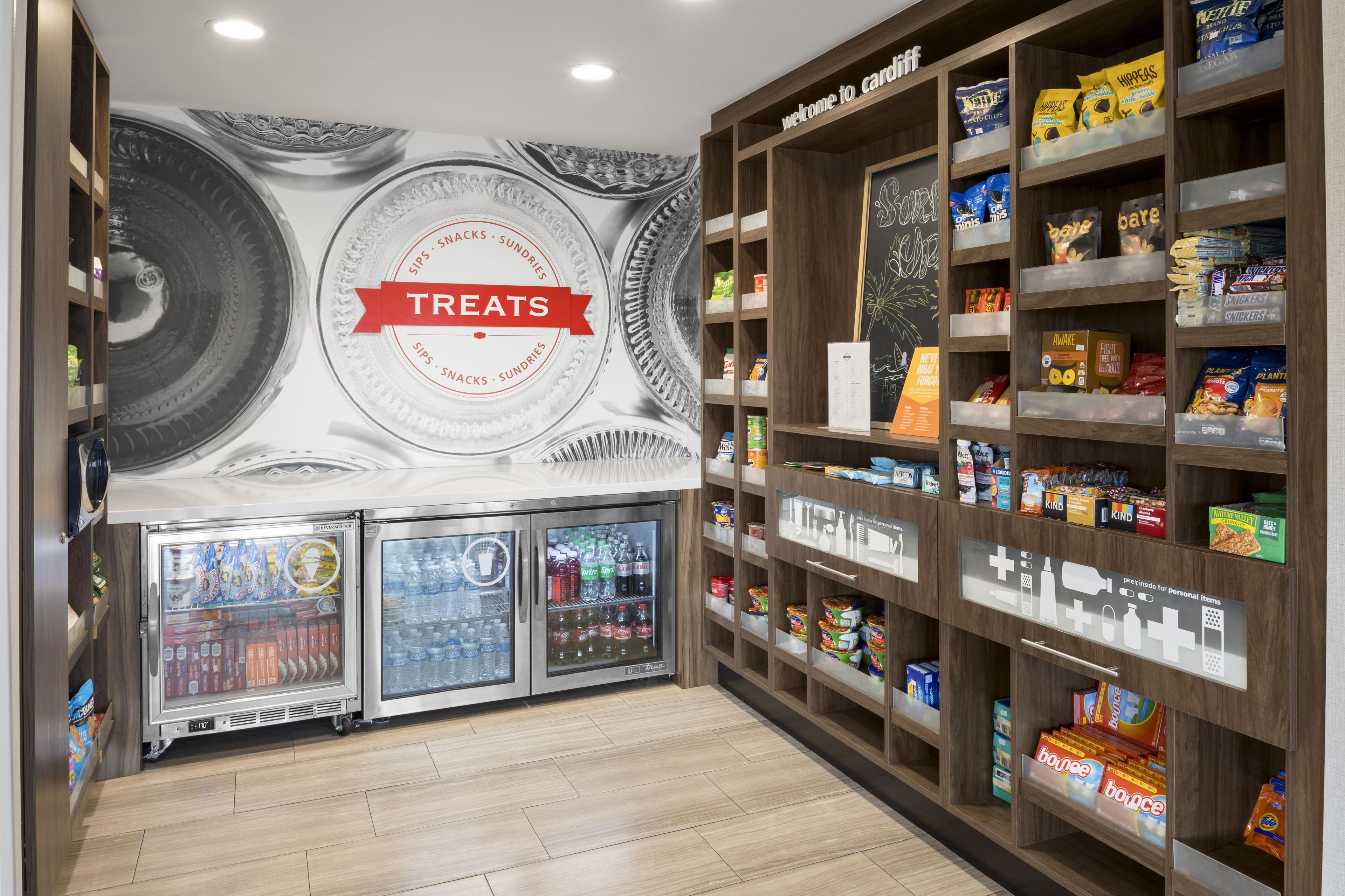 Ein Bereich mit Snacks und Getränken, ein Schild mit der Aufschrift 'Treats', Regale voller Snacks und ein Getränkeautomat.