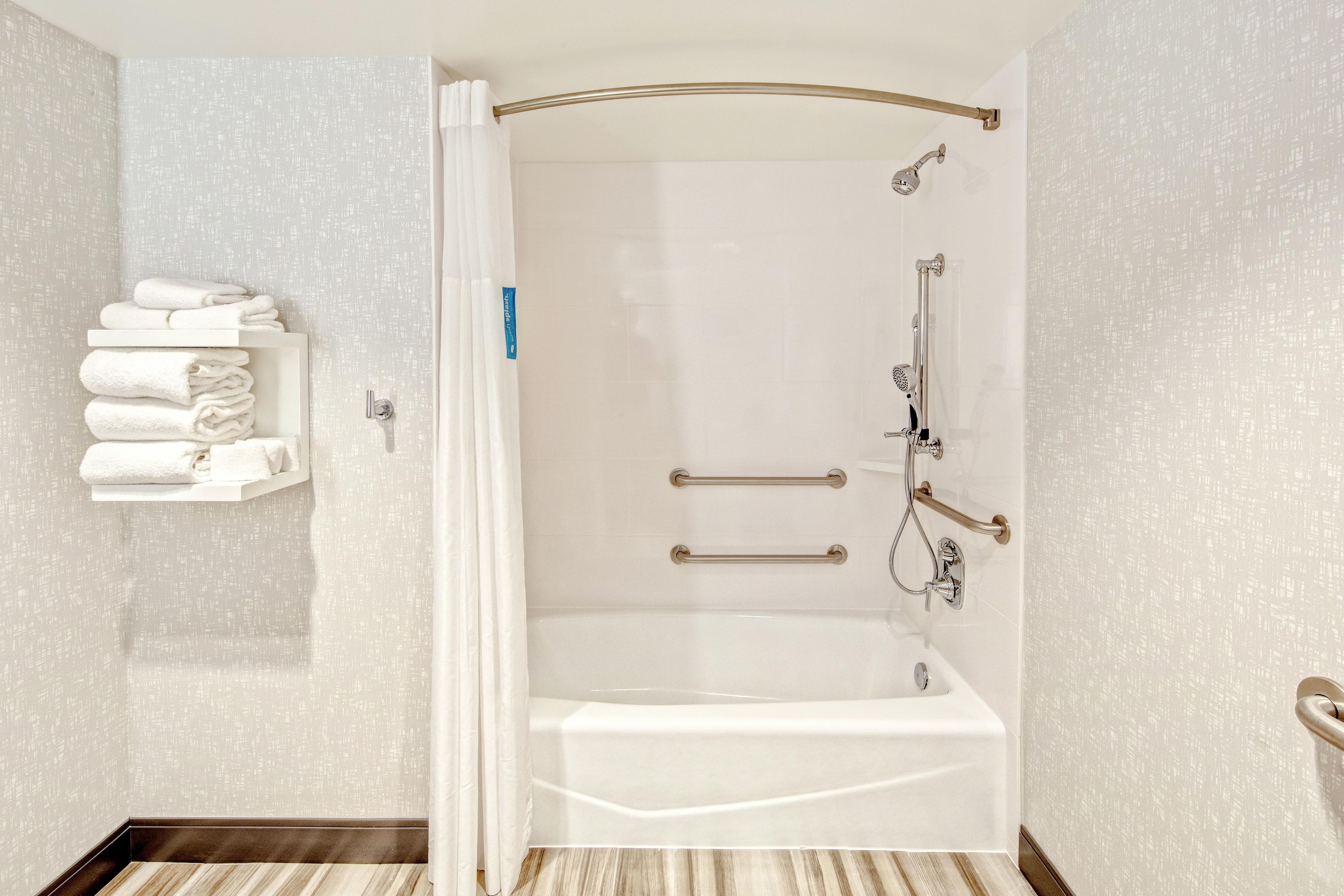 A modern bathroom with a walk-in shower, grab bars, and a towel rack.