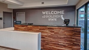A reception desk with a wooden panel design and a digital kiosk, located in a modern hotel lobby with a large window and a welcome sign. - Hampton Inn Cardiff Beach Encinitas, CA Near Del Mar (Cardiff-by-the-Sea)