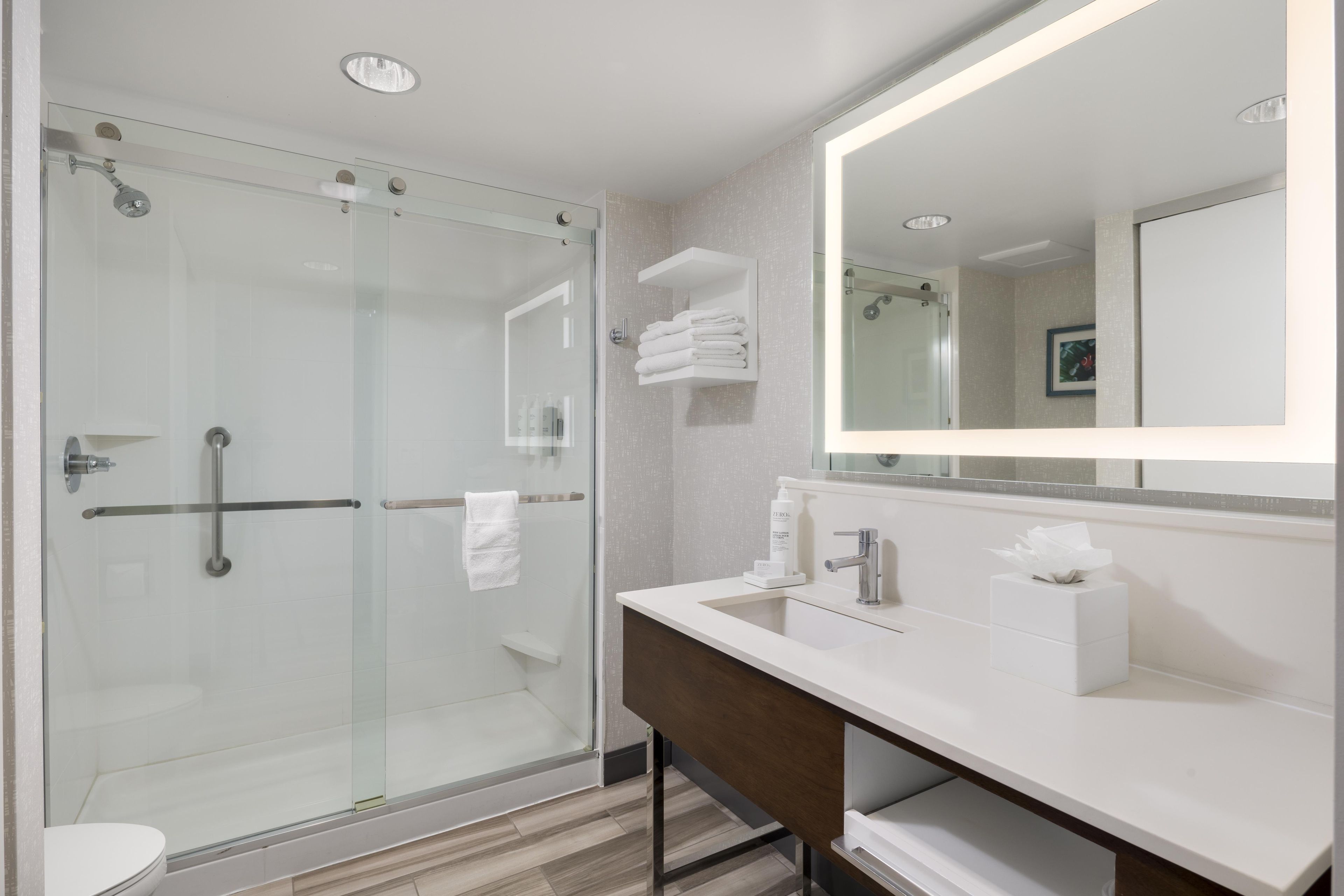 Un baño moderno con ducha acristalada, tocador con espejo y un inodoro.