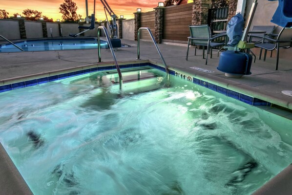 Una piscina con fuente de agua, rodeada por un muro de piedra y un patio con sillas.