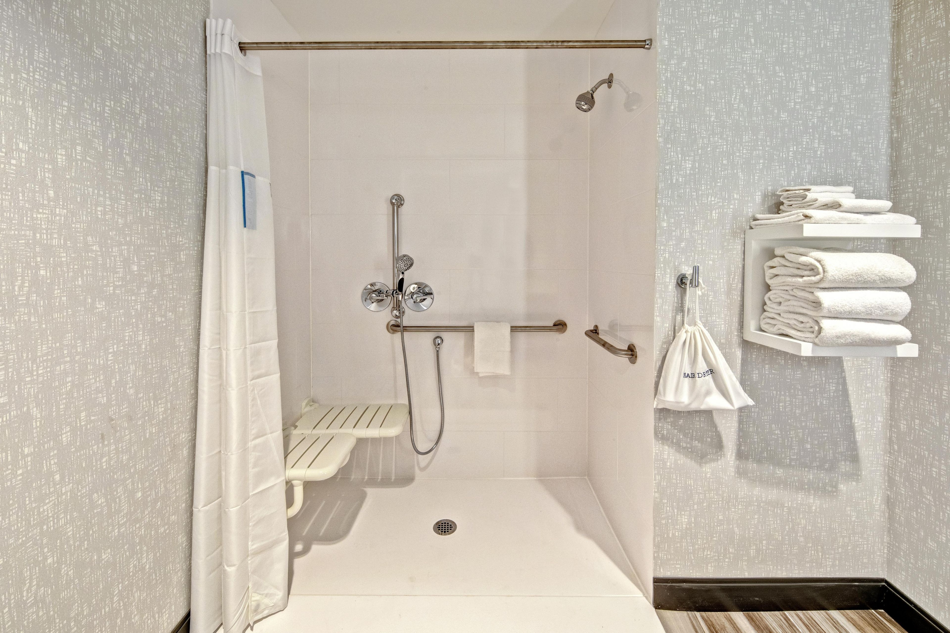 Une douche à l’italienne avec une barre d’appui, un porte-serviettes avec des serviettes pliées et une pomme de douche.