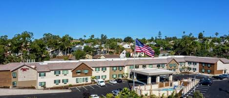A hotel with a parking lot, a flag, and a pool area.
