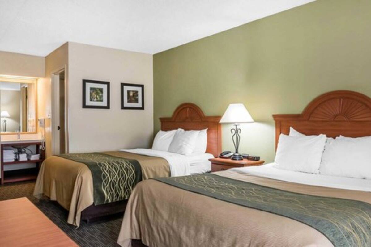A hotel room with two beds, a nightstand with a lamp, a desk with a chair, and framed pictures on the wall.