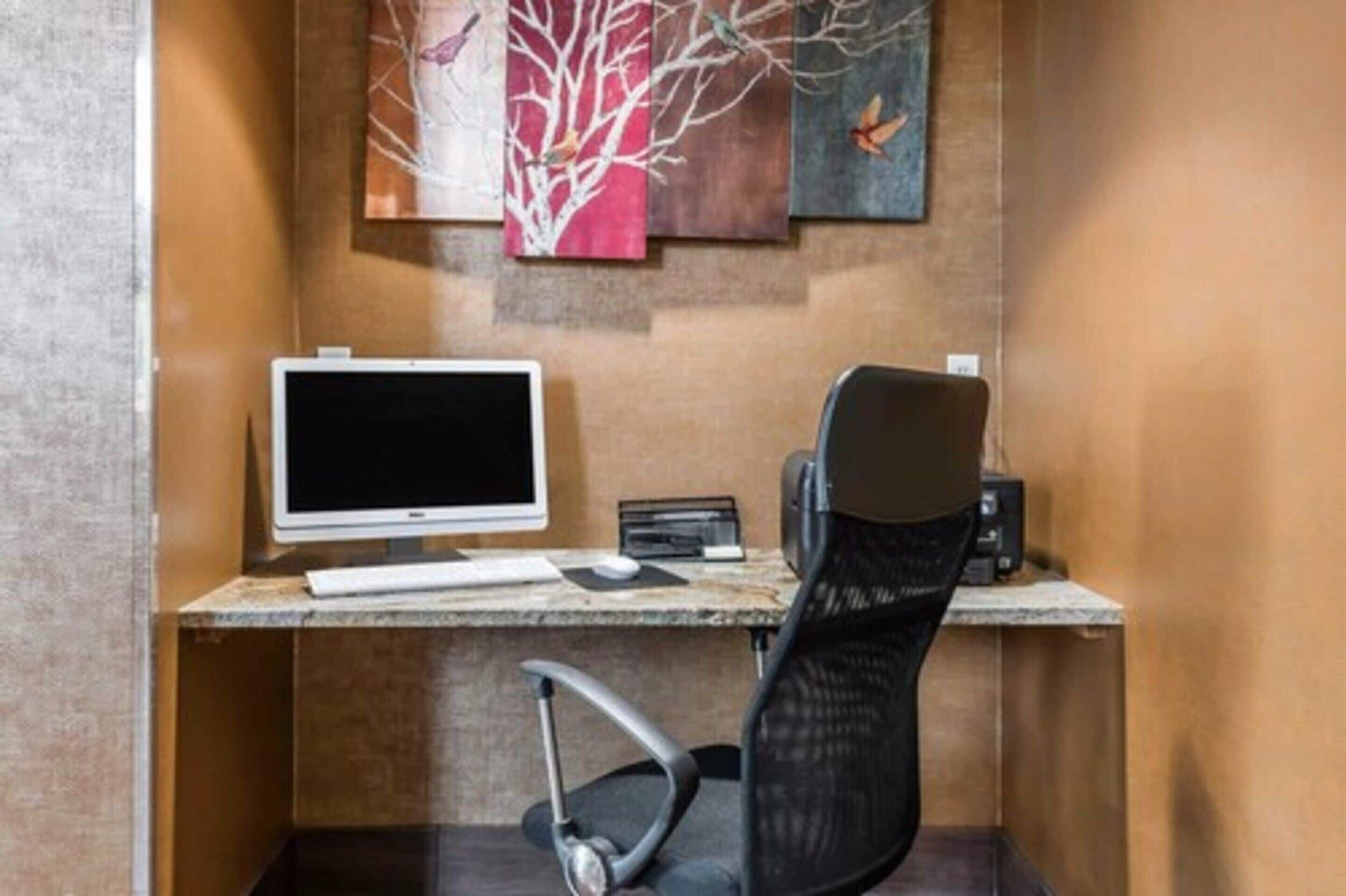 A modern office desk with a computer monitor, keyboard, and mouse, a black office chair, and a small black speaker.