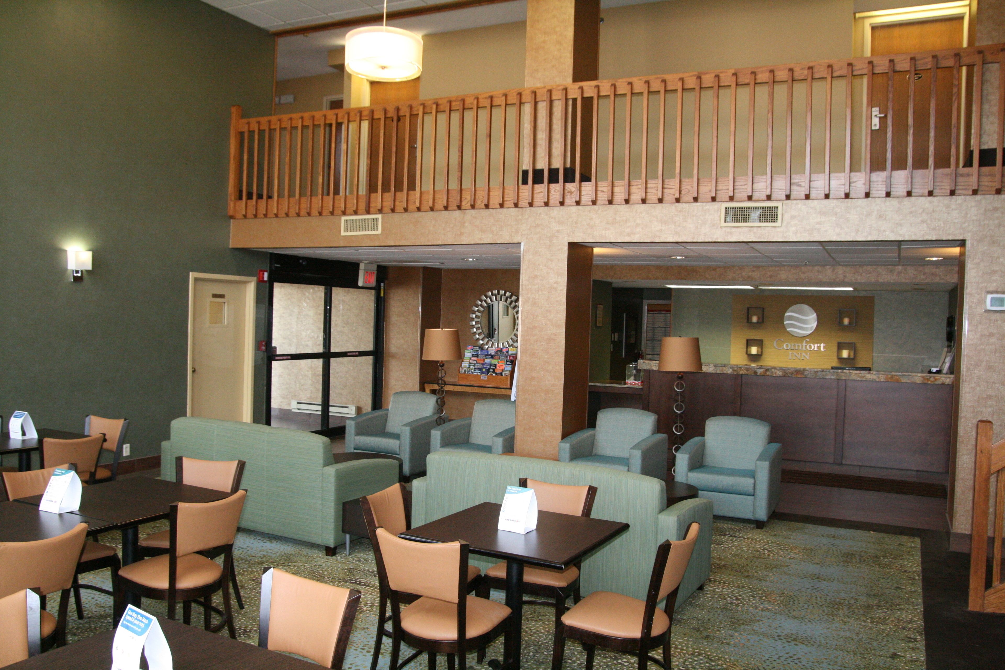 Un vestíbulo de hotel con varias zonas de estar, incluidas mesas y sillas, un mostrador de recepción y un balcón con barandillas de madera.