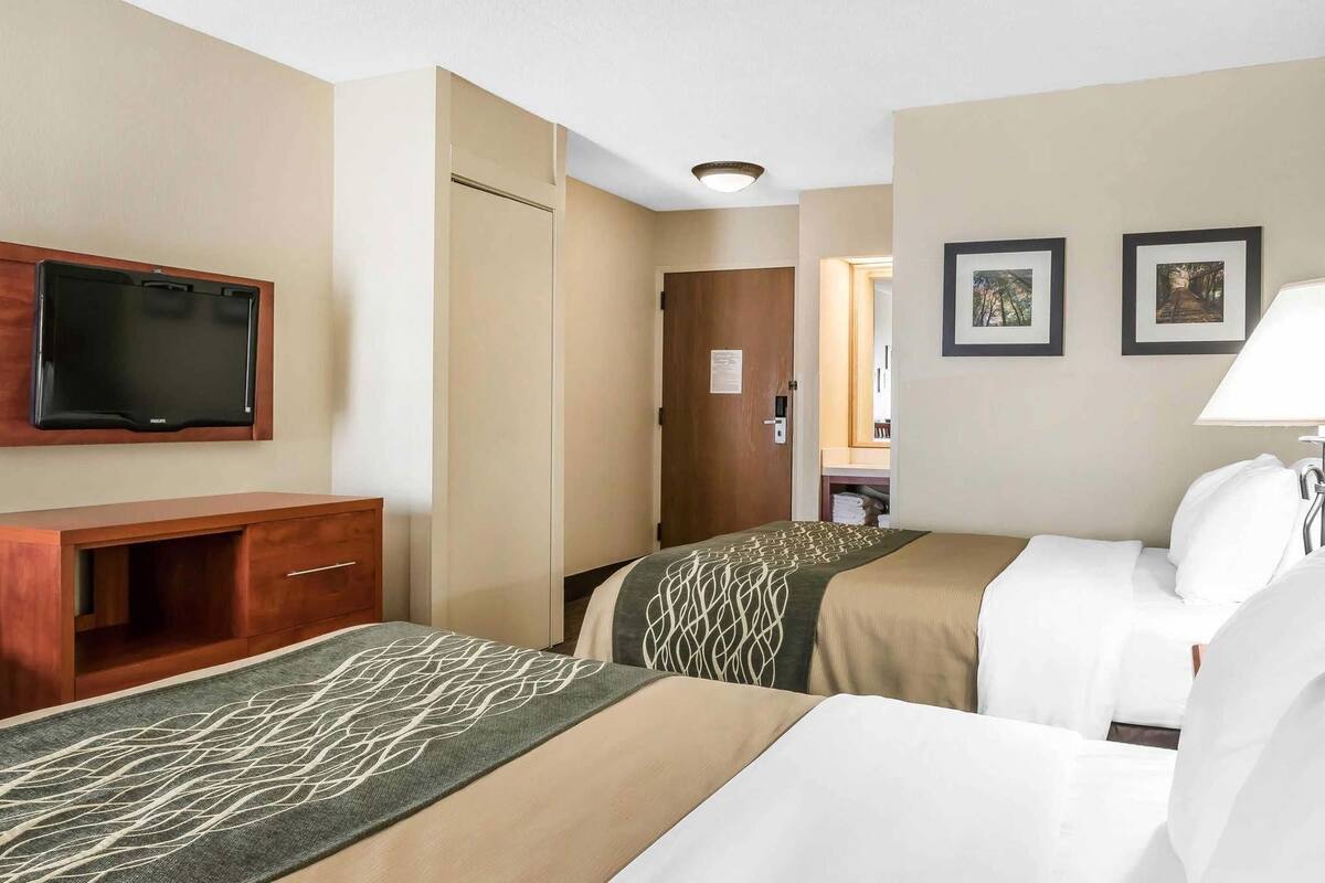 A hotel room with two beds, a TV, a wooden desk, and a door leading to a bathroom.