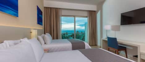 A hotel room with two beds, a desk, a TV, and a balcony with a view.