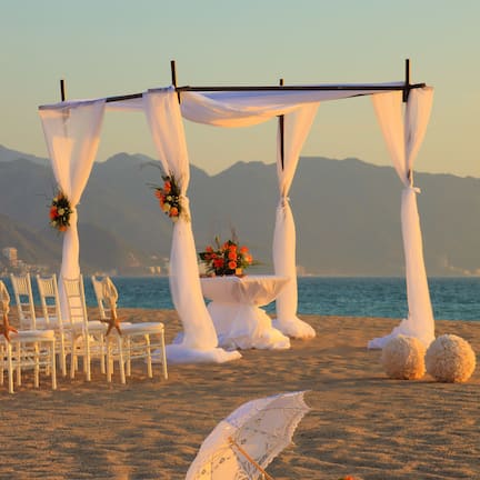 A beach wedding setup with white chairs and a canopy, a table with flowers, and a decorative umbrella.