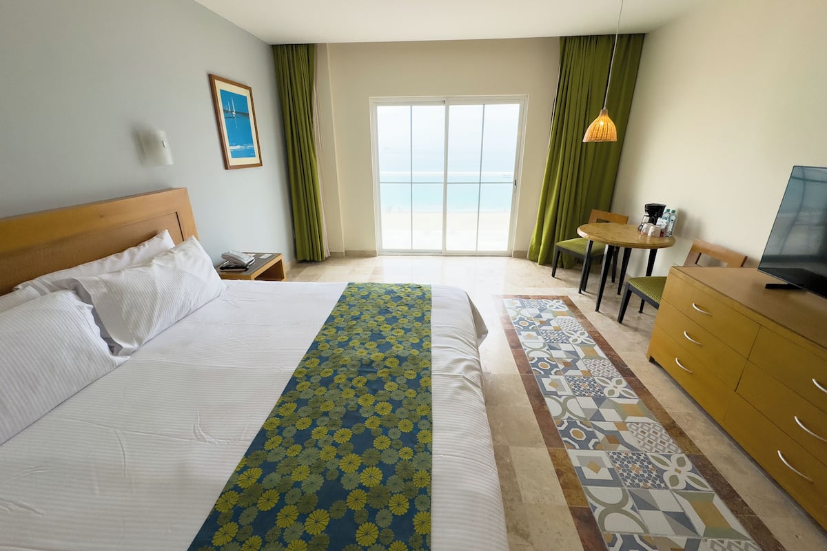 Habitación de hotel con una cama, un escritorio, un televisor y vistas al océano por la ventana.
