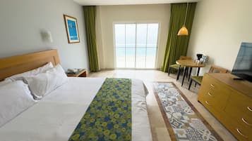 Quarto de hotel com cama, escrivaninha, televisão e vista para o oceano pela janela.