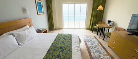 Ein Hotelzimmer mit Bett, Schreibtisch, Fernseher und Meerblick durch das Fenster.
