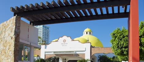 Entrada de hotel con pérgola, muros de piedra y una cúpula amarilla.