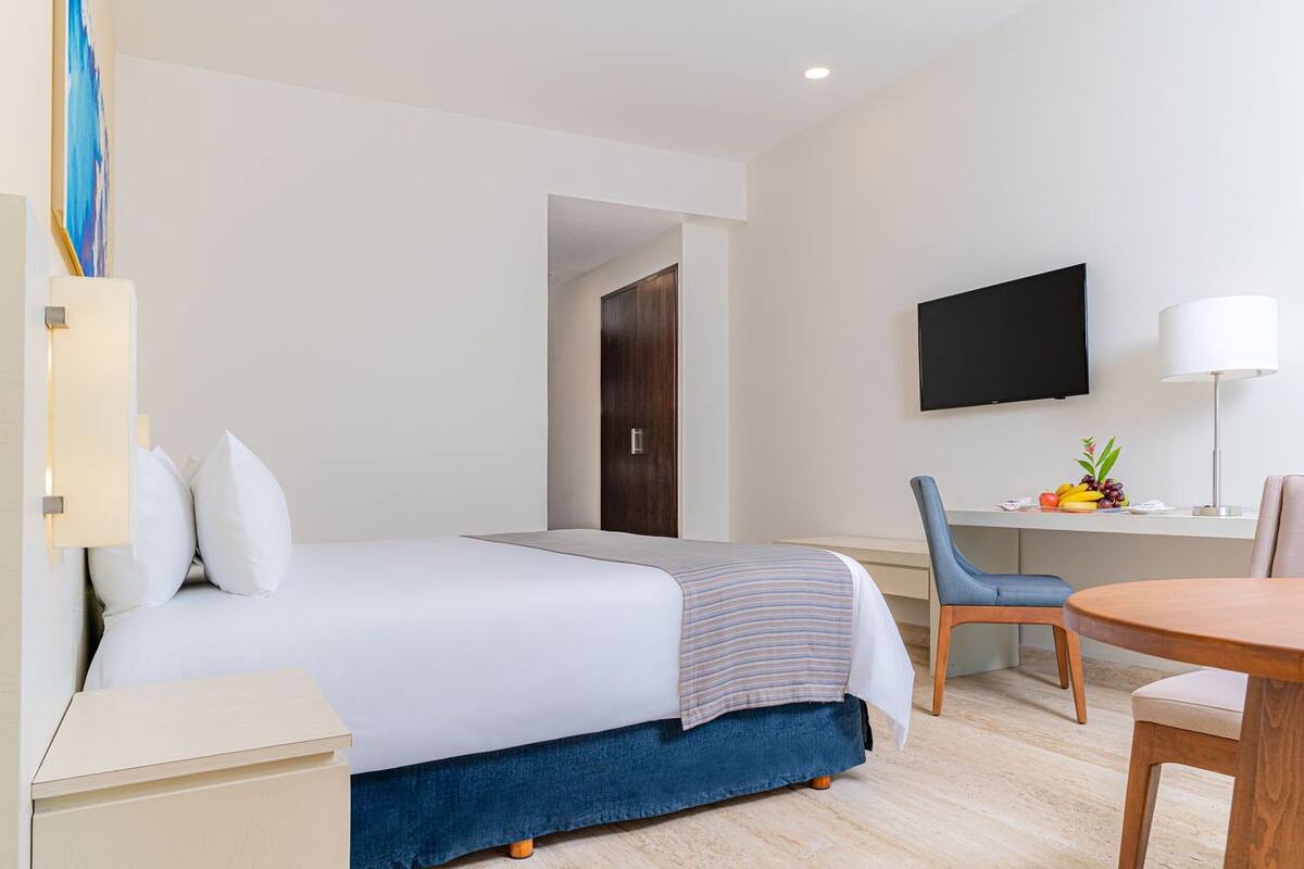 Una habitación de hotel con cama, escritorio, silla, televisor y lámpara.