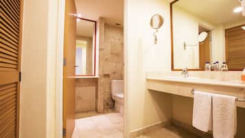A bathroom with a toilet, sink, and mirror. There are towels hanging on the wall and a shower visible in the background.