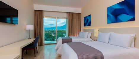 A hotel room with two beds, a desk, a chair, a TV, and a large window with a view of the mountains.
