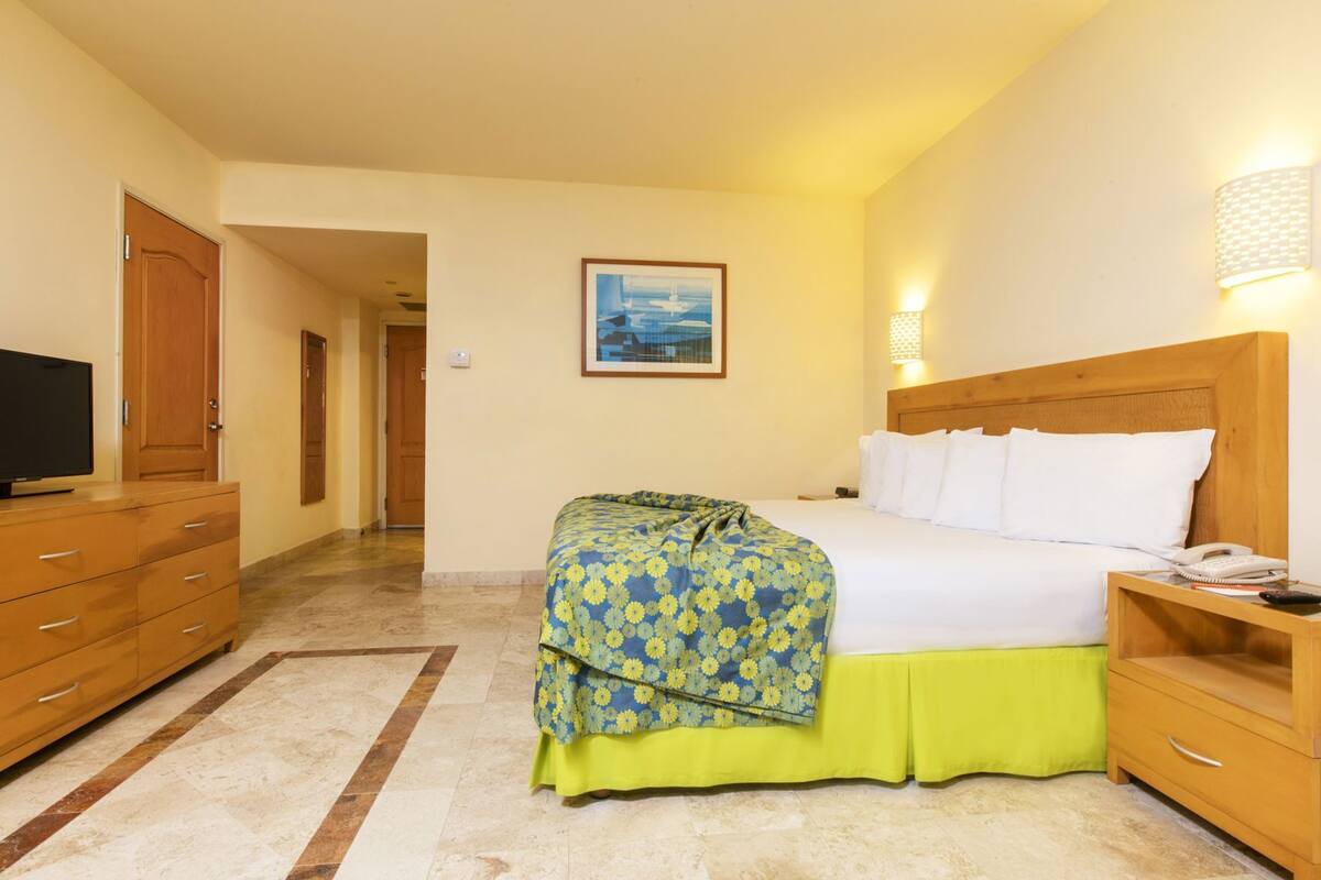 Habitación de hotel con cama, televisión, mesita de noche con teléfono y un cuadro en la pared.