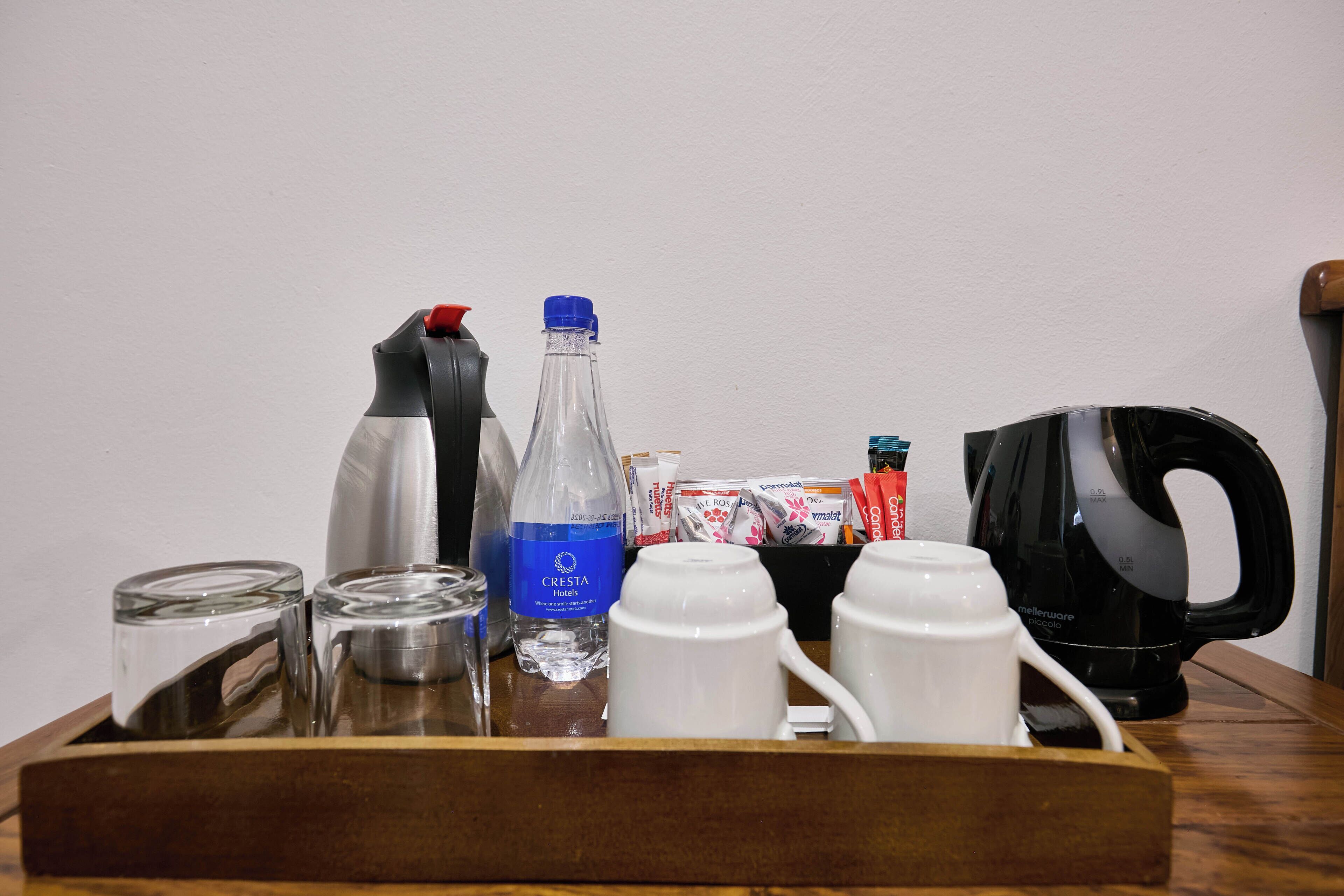 A tray with a water bottle, a silver container, a black pitcher, white cups, and a black coffee maker.