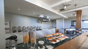 Un área de bufé con diferentes opciones de comida, una estación de café y una cocina al fondo.