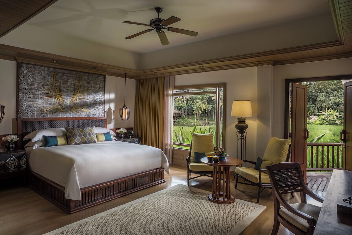 A spacious bedroom with a large bed, a ceiling fan, and a view of a lush garden.