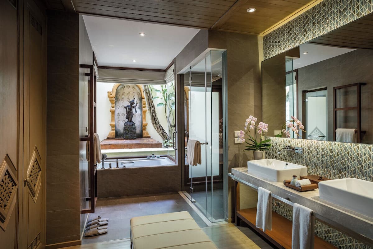 A modern bathroom with a large mirror, two sinks, a shower area, and a decorative statue.