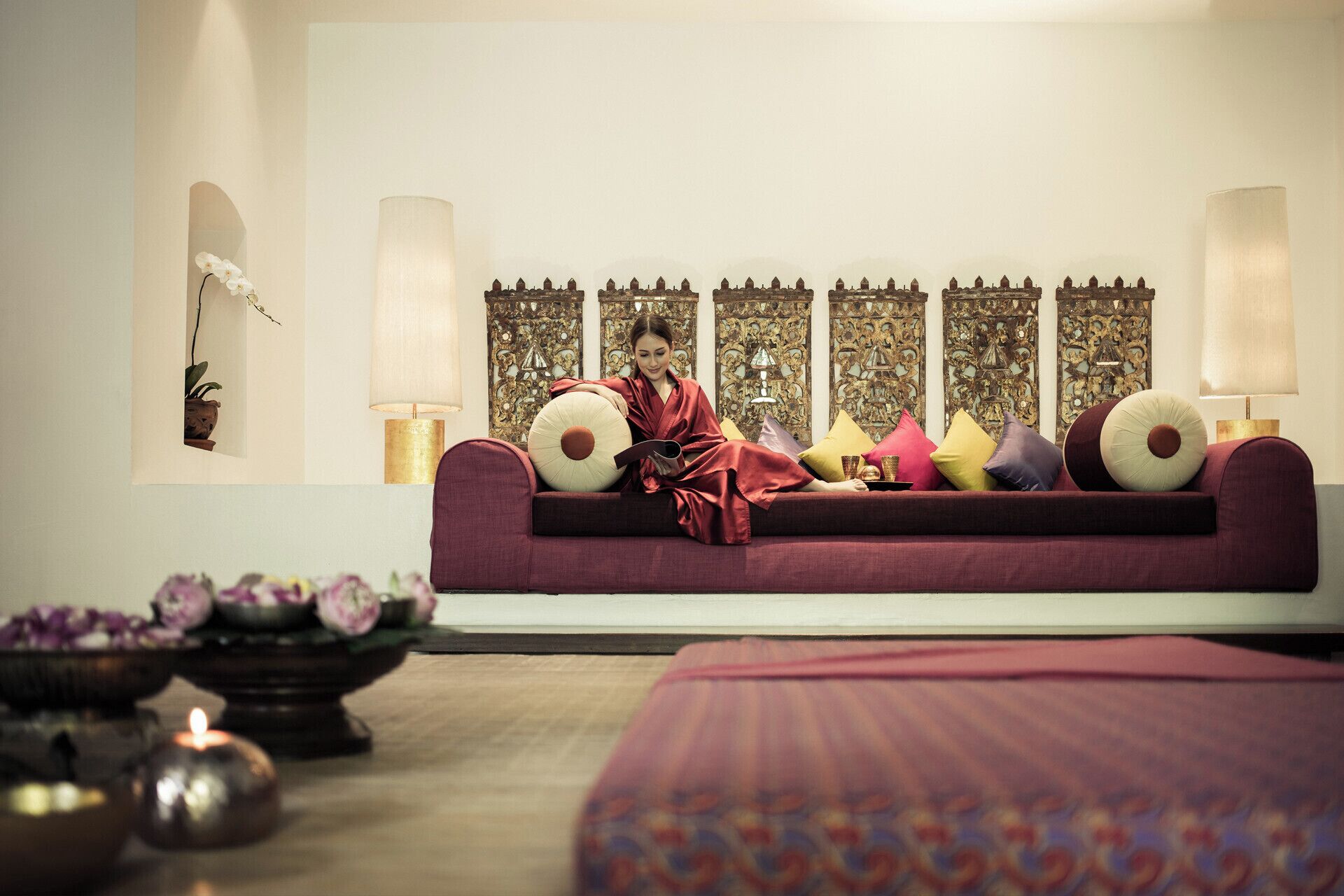 A room with a sofa, decorative pillows, wall art, and a small table with flowers.