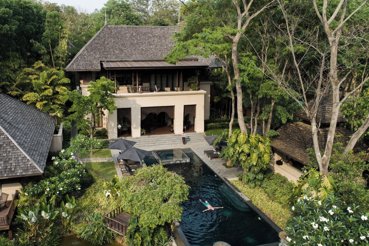 A large house with a swimming pool surrounded by lush greenery.