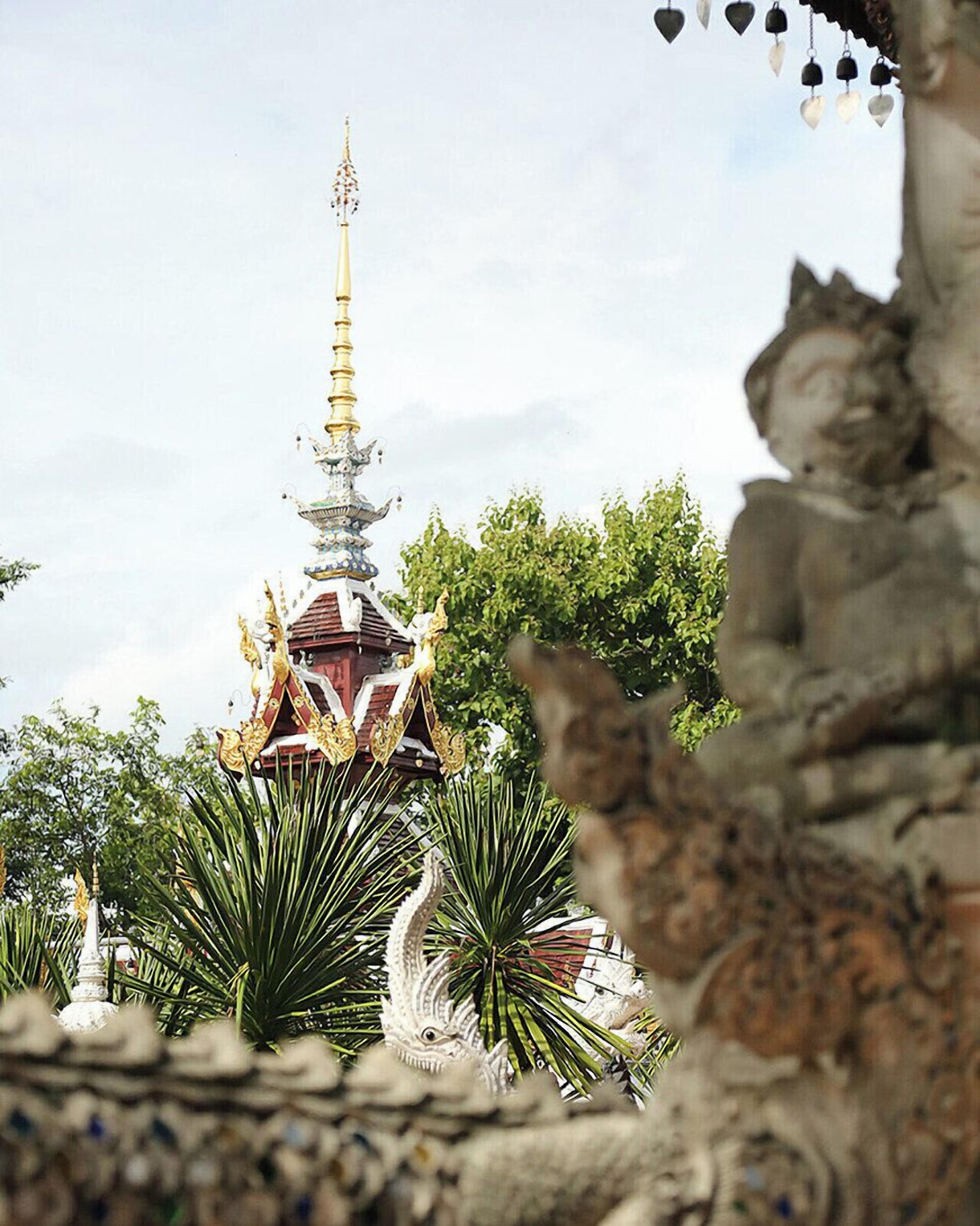 Um templo com uma torre alta, cercado por vegetação e construções de pedra.