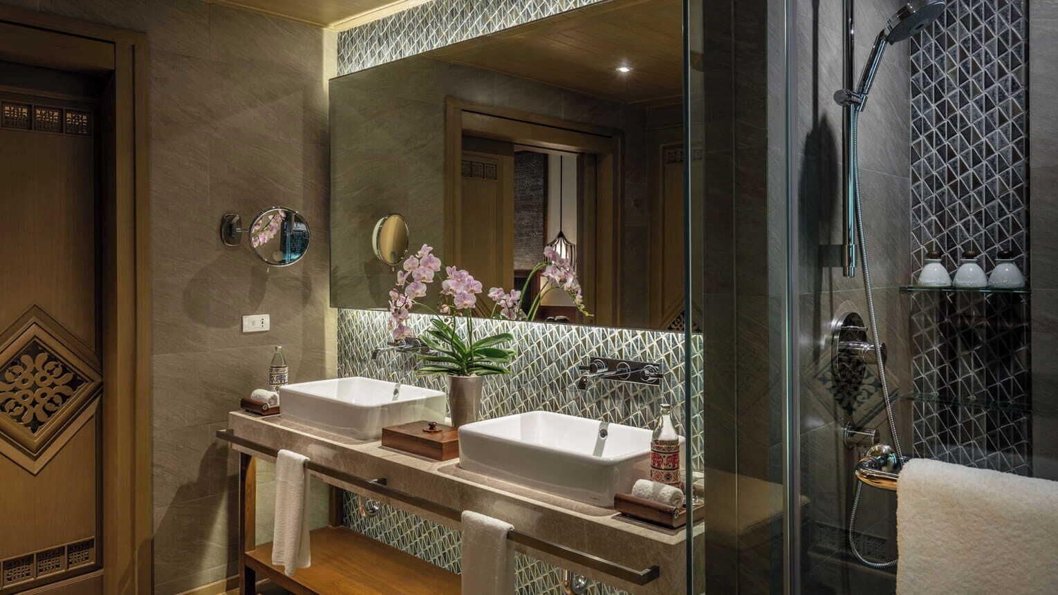 A modern bathroom with two sinks, a large mirror, and a shower area.