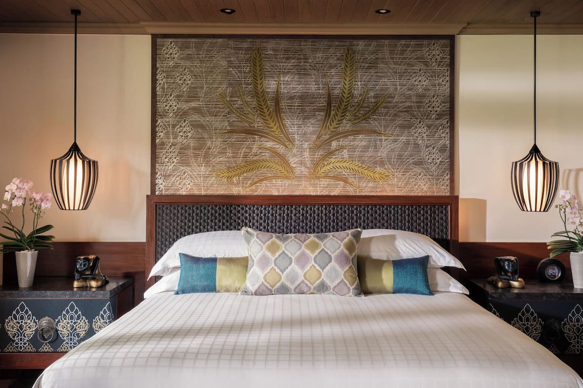 A hotel room with a large bed, two bedside tables, decorative wall panels, and hanging pendant lights.