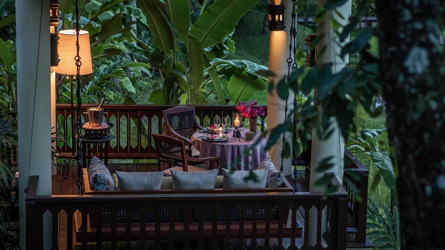 Un espacio al aire libre con mesa y sillas, rodeado de abundante vegetación.