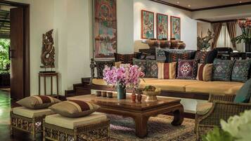 A traditional living room with a sofa, coffee table, and wicker chairs. There are decorative pillows, a vase with flowers, and a Buddha statue.