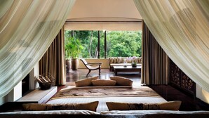 Een slaapkamer met een groot bed, een sofa en uitzicht op een weelderige tuin.