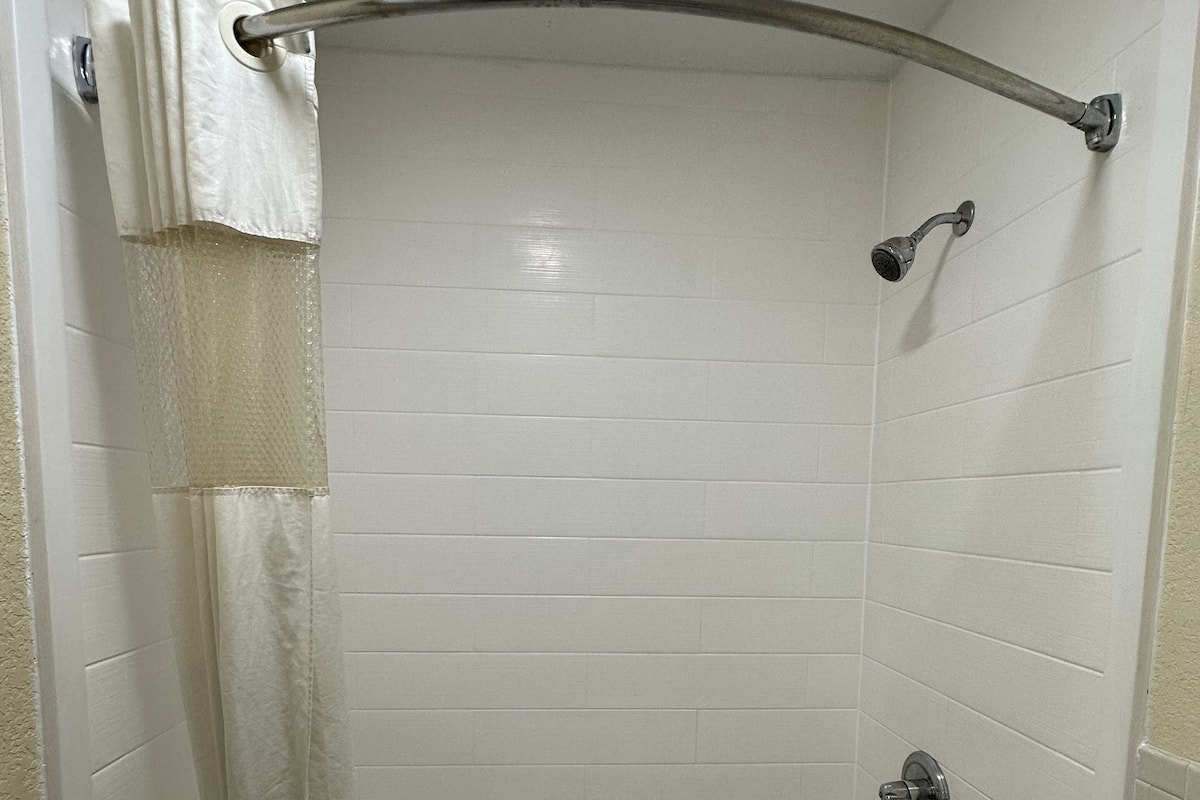 A corner shower with white tiles, a chrome showerhead, and a towel rack.