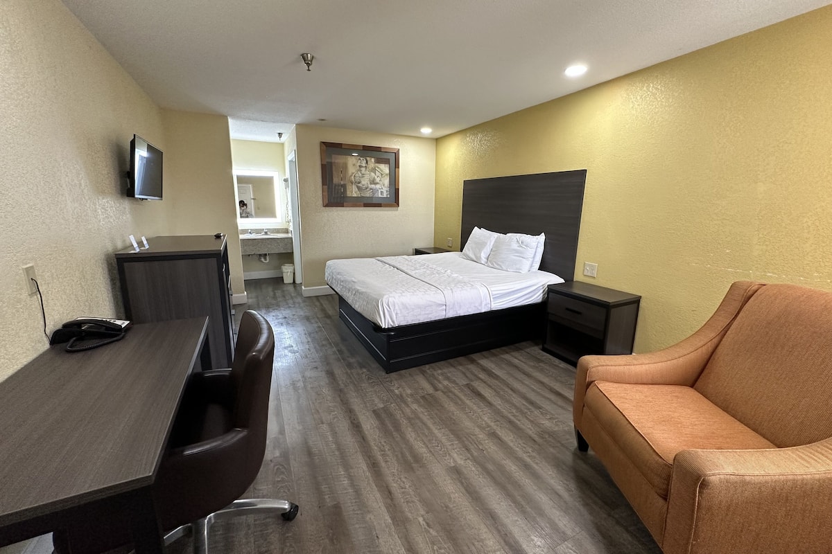 A hotel room with a bed, desk, chair, and a sofa.