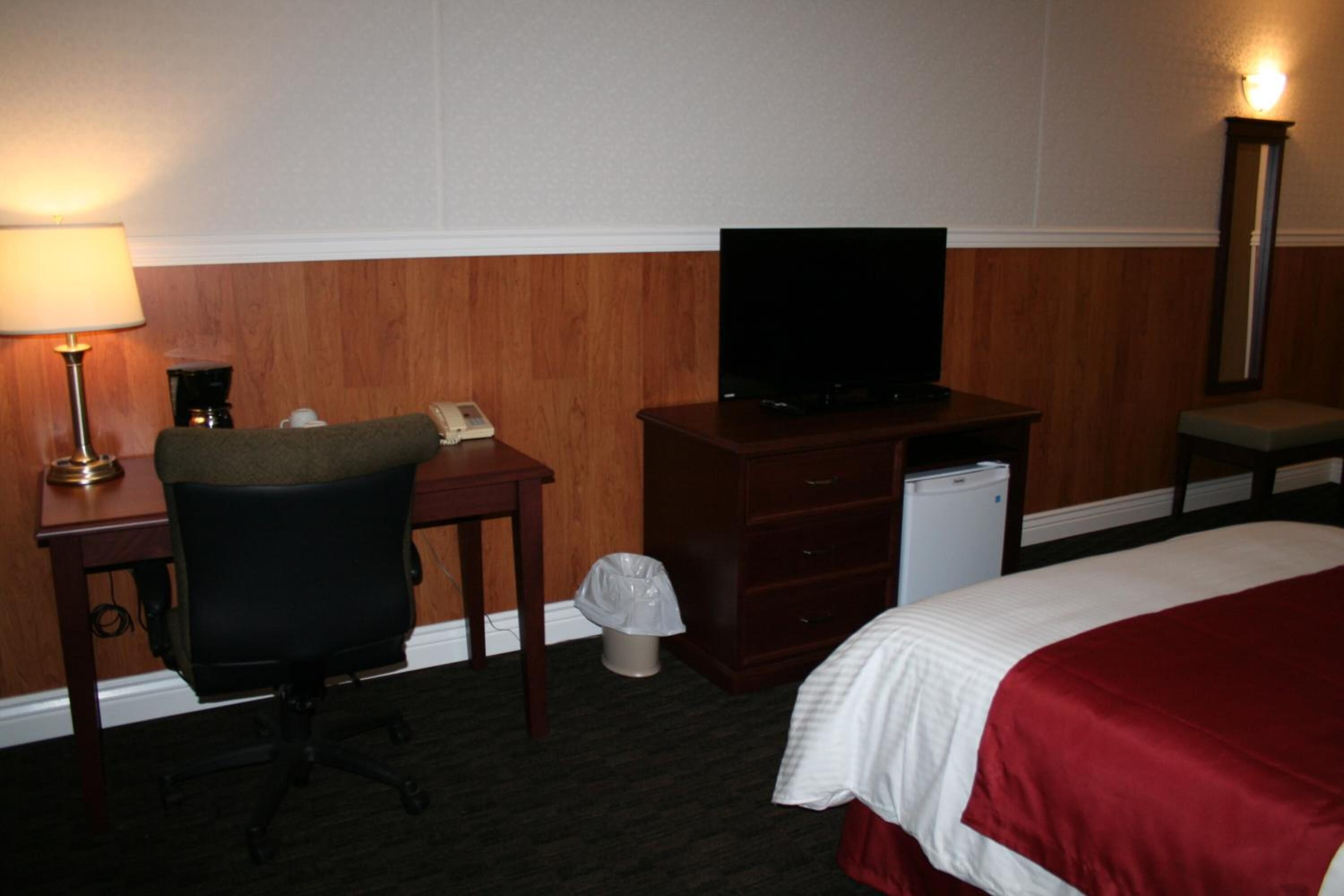 Ein Hotelzimmer mit Bett, Schreibtisch mit Stuhl, Fernseher, Mülleimer und Lampe.