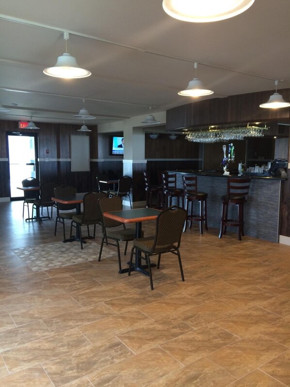 Un restaurante con zona de bar, varias mesas y sillas, y una pantalla de televisión.