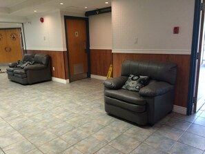A lobby with two leather recliners, a wooden door, and a sign indicating a restroom. - Hotel North (North Sydney)
