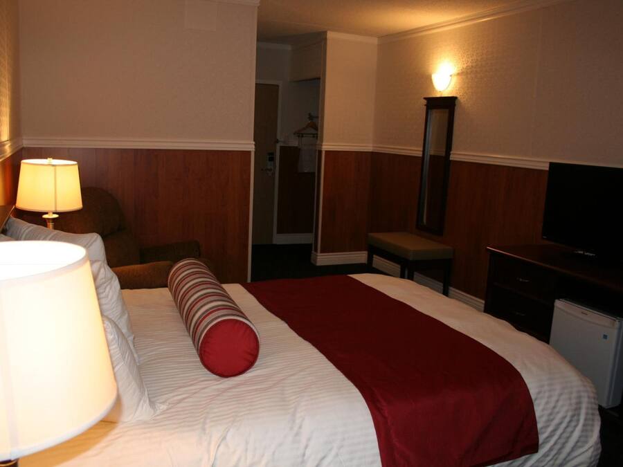A hotel room with a bed, a desk, a chair, a lamp, a television, and a mirror.