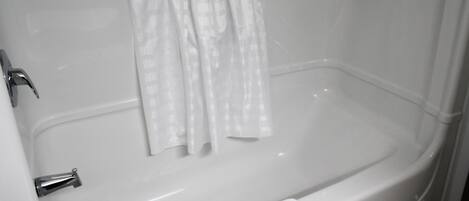 Una bañera blanca con cortina de ducha, una toalla y un grifo.