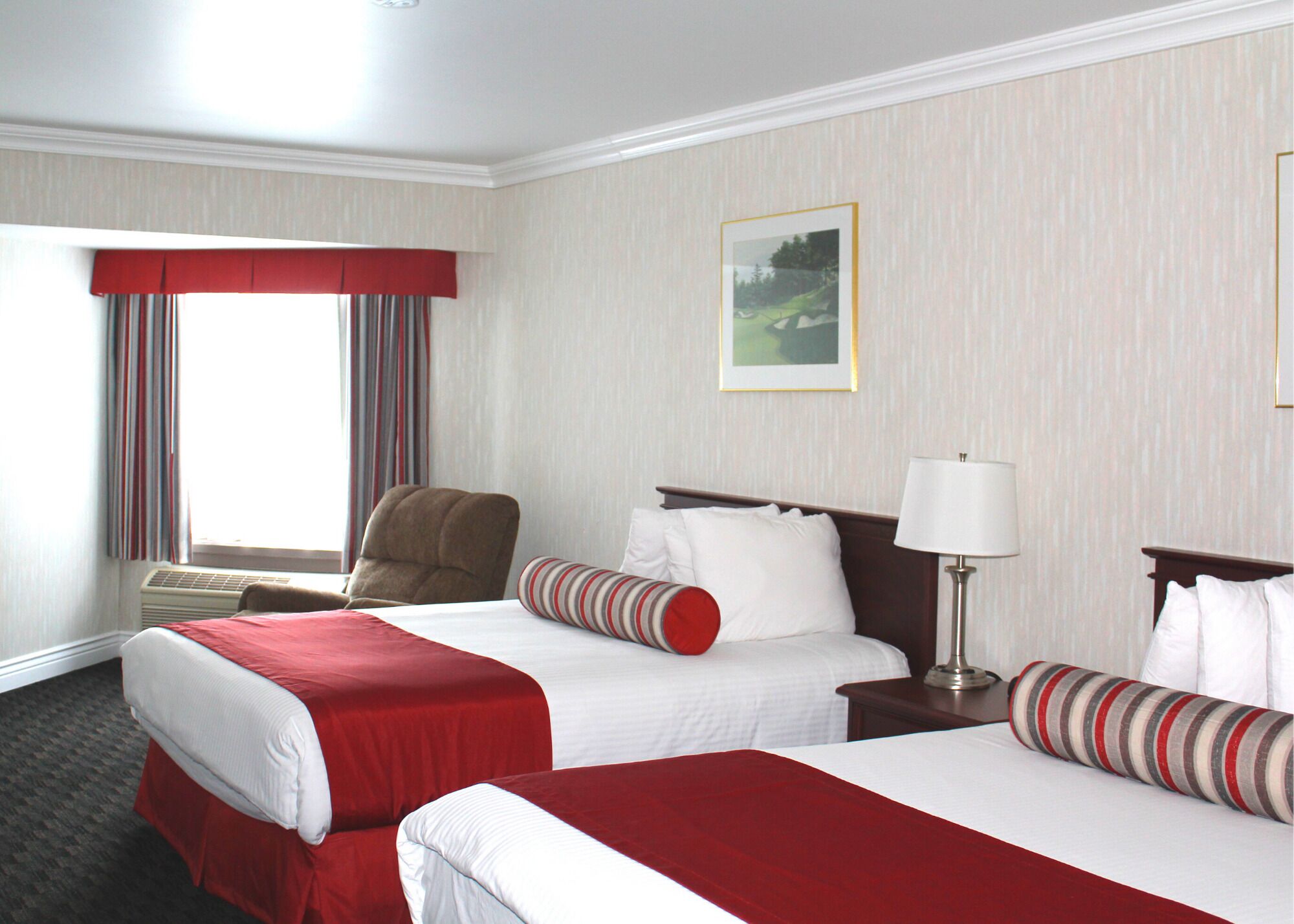 Ein Hotelzimmer mit zwei Betten, einem Sessel, einer Lampe und einem Fenster mit Vorhängen.
