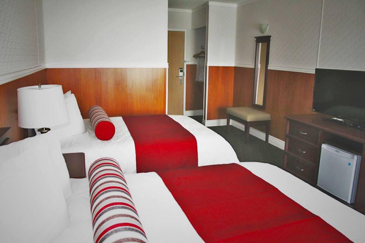 Ein Hotelzimmer mit zwei Betten, einem Schreibtisch, einem Fernseher und einem Spiegel.
